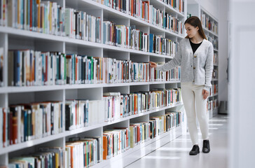 Woman in library, student search for book and research project, reading with education and learning at university campus. Knowledge, story and fiction with textbook, study and browsing bookshelf - obrazy, fototapety, plakaty