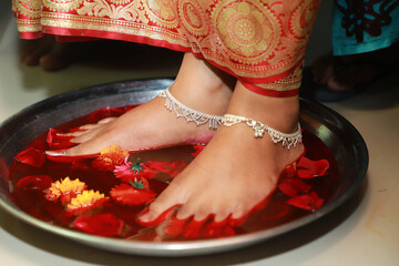 Fototapeta premium Griha Pravesh Concept - feet of a Newly married Indian Hindu bride in Saree stepping in a plate filled with liquid kumkum before entering husband’s house for the first time