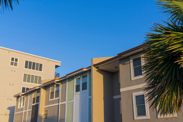 Exterior view of home on a sunny day in Destin Florida residential neighborhood. The houses has small glass paned windows and sunlit walls against clear blue sky and trees.