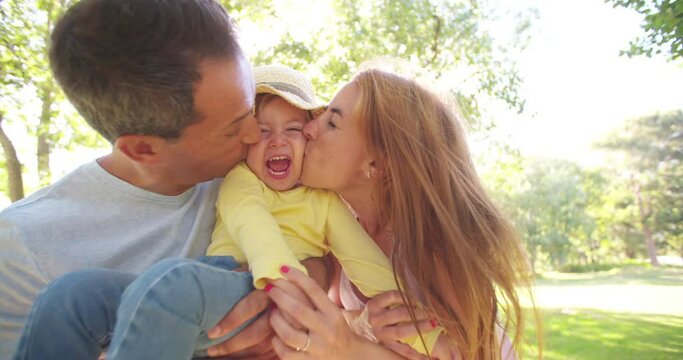 Happy parents affectionately kissing their little toddler girl on both sides of her face in slow motion