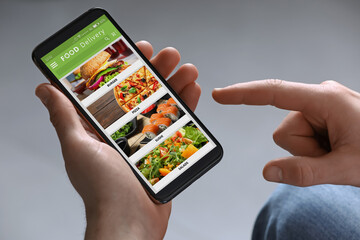Food delivery service. Man choosing dish from menu on site using smartphone on light grey...