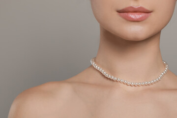Young woman wearing elegant pearl necklace on grey background, closeup. Space for text