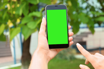 Woman using smartphone with green screen outdoors, closeup. Gadget display with chroma key. Mockup for design