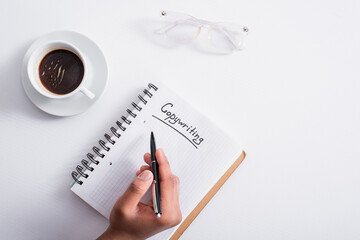 Top view of man holding pen near notebook with copywriting lettering and coffee on table.