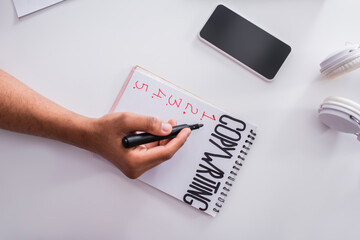 Top view of copywriter holding marker near notebook and cellphone at home.