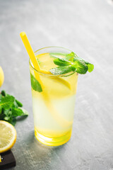 Lemonade drink or mojito cocktail in a glass with straw, lemon fruit and mint leaves, refreshing summer beverage