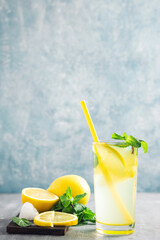 Lemonade drink or mojito cocktail in a glass with straw, lemon fruit and mint leaves, refreshing summer beverage