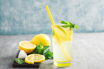 Lemonade drink or mojito cocktail in a glass with straw, lemon fruit and mint leaves, refreshing summer beverage