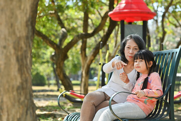 Happy senior grandmother having fun enjoying talk with cute little grandchild in the park on a sunny day.