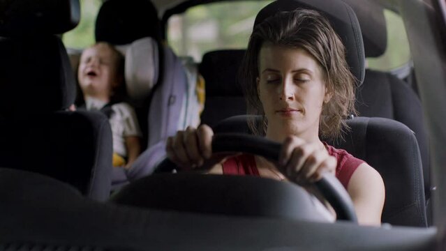 Handheld shot of mother sleeping on vehicle seat while son playing in background