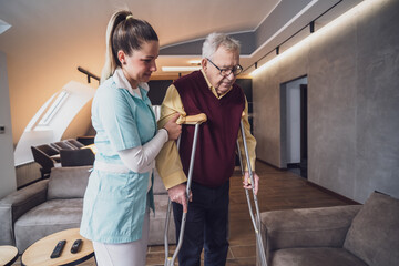 Nurse home caregiver is assisting old man at his home. Professional health support for elderly people.