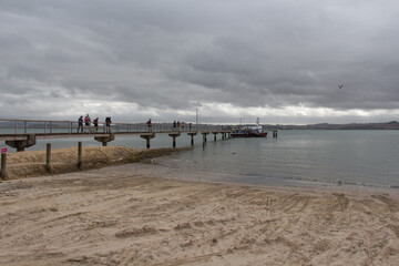 People walking on wharf towards cruise ship, Shelly Beach, Kaipara Harbour, New Zealand.