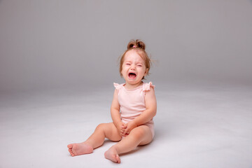 a baby girl in a pink bodysuit is sitting crying on a white background