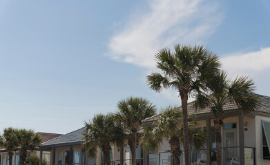 Houses with clay roof tiles and balconies in Destin, Florida. There are views of palm trees at the front of balconies of single-family homes against the sky background.
