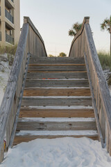 Wooden stairs on a white sand over sand dunes at Destin, Florida. White sand at the bottom of the stairs with railings near the building on the left in a vertical shot view.