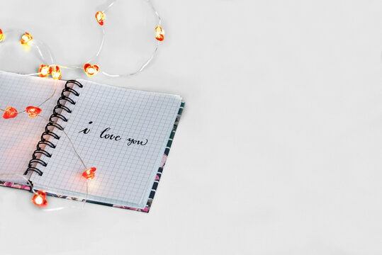 I love you romantic note in notepad covered with a heart-shaped light chain isolated on white background with copy space. Great Valentine's design concept for backgrounds, wallpapers, posts, aposters.