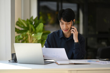 Handsome male financial advisor looking at document and talking on mobile phone with client