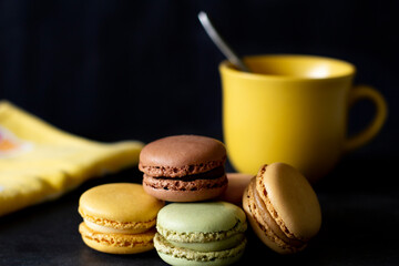Macarons, yellow cup and napkin on black background.