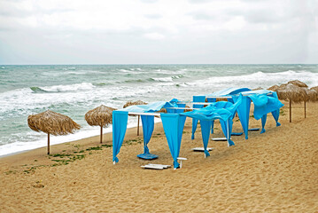 Deserted beach. Empty sun loungers next to the stormy sea