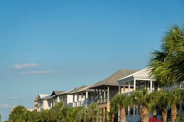 Rows of palm trees at the front of houses against the sky at Destin, Florida. There are houses with balconies under the blue sky background.