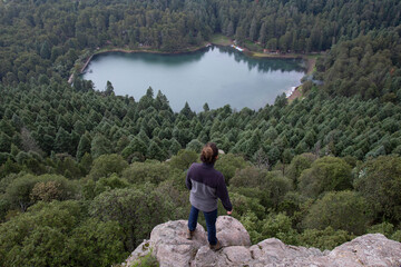 Naklejka premium Male hiker standing on the edge of cliff, admiring a forest and lake