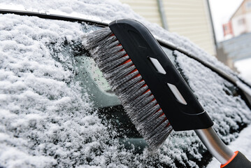 Cleaning and clearing car with brush from snow in winter.