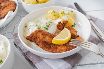 Breaded chicken schnitzel with kohlrabi vegetable with bechamel sauce and boiled potatoes on a plate. Homemade cooked