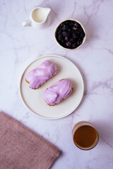 eclair in purple berry glaze and coffee with milk in a glass