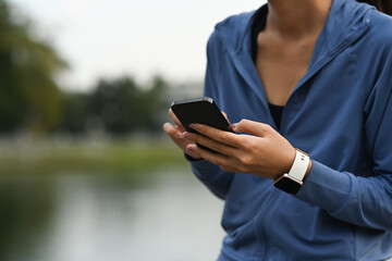 Cropped view of woman in sportswear using smart phone, resting after running in the green park