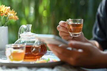 Cropped shot of man holding a cup of tea and using smart phone against blurred nature background
