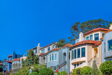 Fototapeta na wymiar Houses in San Francisco neighborhood with blue sky on a sunny day. The homes have colorful exterior walls and ourdoor stairway leading to the intreior of the residence.