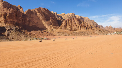 Large convey of tour trucks and jeeps in Arabian Wadi Rum desert landscape with mountains of Jordan, Middle East