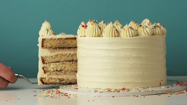Woman cut out a slice of a birthday cake using knife and spatula. Blue background. Homemade festive pastry. Layered sponge bisсuit cake with cream cheese filling. Happy birthday concept