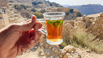 Clear glass cup of delicious sweet mint tea overlooking Arabian desert mountainous landscape in Jordan, Middle East 