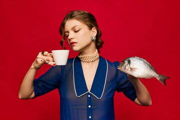 Delicious weird taste. Young extravagant woman with cup of coffee and raw fish on bright red...