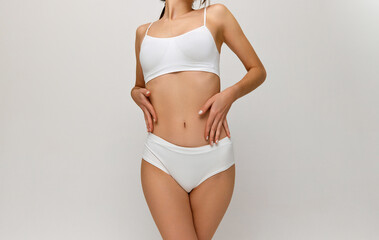 Fototapeta na wymiar Dieting. Cropped image of slim healthy female body, breast, belly over grey studio background. Model posing in white underwear. Concept of body and skin care, fitness, natural beauty, health, wellness