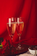 Glasess of champagne in front of red bacground. Romantic seasonal Valentine holiday with roses, candies. Vertical photo