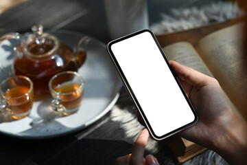 Woman holding smart phone against traditional tea set with cups and teapot on rustic wooden table