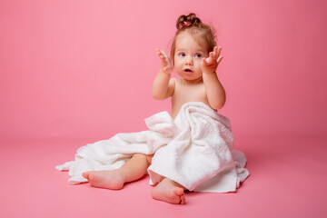 Obraz na płótnie Canvas baby girl in a diaper wrapped in a towel sitting on a pink background, bathing concept