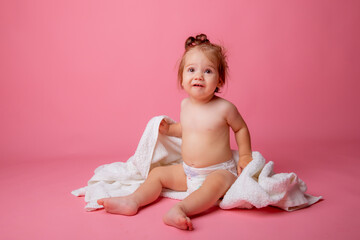 baby girl in a diaper wrapped in a towel sitting on a pink background, bathing concept