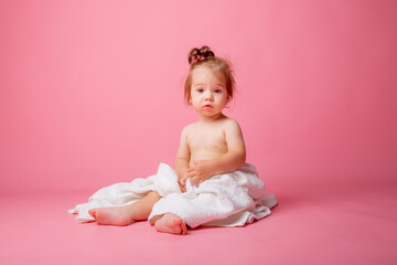 baby girl in a diaper wrapped in a towel sitting on a pink background, bathing concept