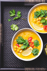 
Light orange veggie curry with chickpeas, chili peppers, coriander leaves and cumin seeds on a wicker ethnic tray. Vegetarian recipes, healthy food. Fusion cuisine
