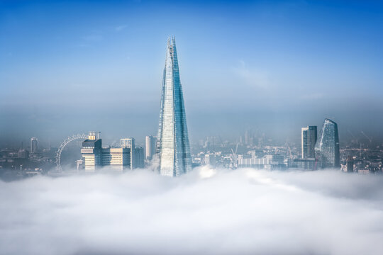The top of the Shard Building at London Bridge and London Eye next to it peaking our of the clouds and fog