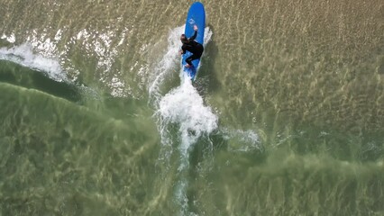 Topdown of Surf professor gives little push while surf student catching small shore wave