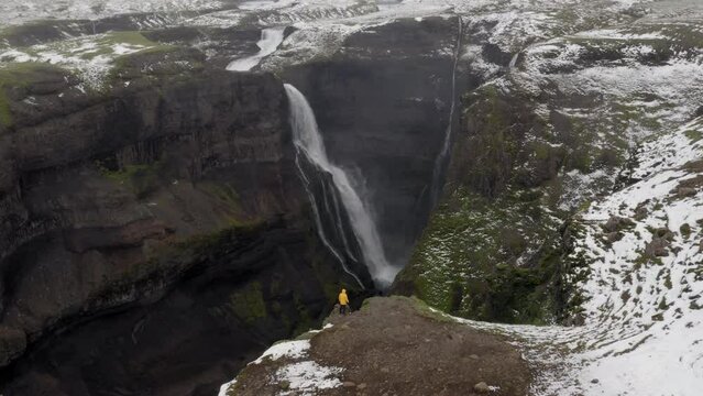 Aerial: Flyover one person wearing yellow jacket, looking at Granni waterfall in Iceland