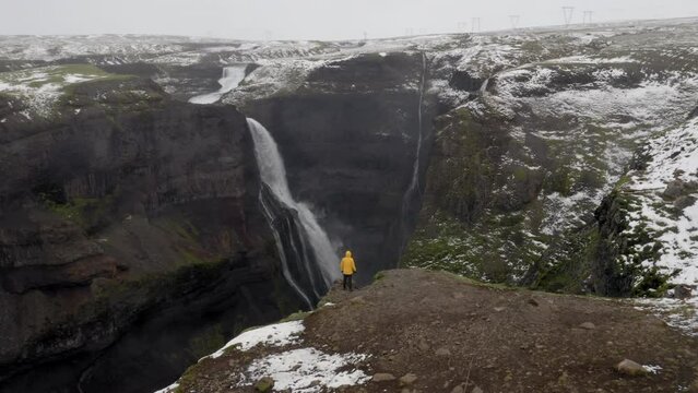 Aerial: Slow panning shot of a man standing near the edge of a cliff, between Haifoss and Granni waterfalls in Iceland