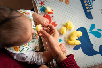 Top view of mother hand and baby sitting at the table, and giving him food. close up. The concept of feeding and weaning baby from the breast. Hispanic family