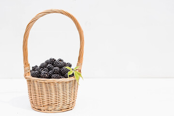 Naklejka na ściany i meble A small wicker basket with fresh blackberries on a white wooden isolated background. A beautiful, healthy ripe summer berry.