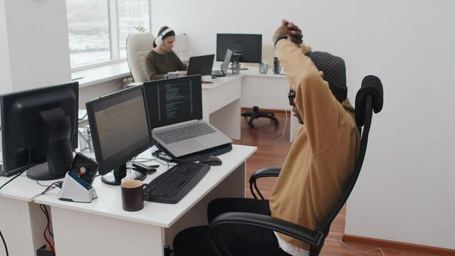 Slow motion of young African American man working on code feeling tired sitting in front of computer for hours doing some stretching and going on working