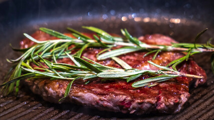 Beef steak frying on a pan with rosemary. Closeup